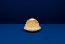 A white, unglazed chinese porcelain tealight candle holder with a dome top and a hole in the top for ventilation, displayed against a dark blue background.